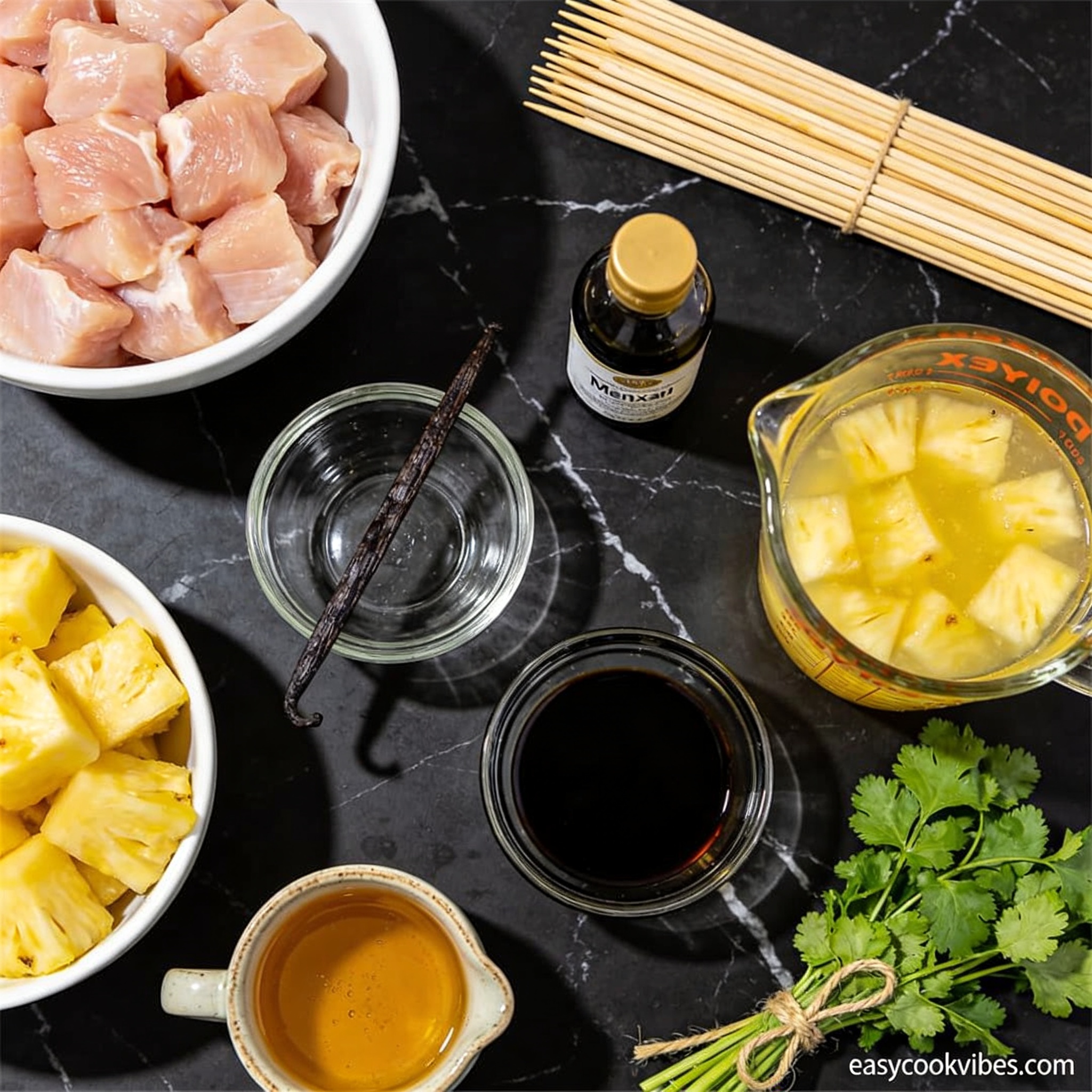 Raw ingredients for gluten free grilled chicken and pineapple skewers with vanilla arranged in white bowls and glass containers on black marble